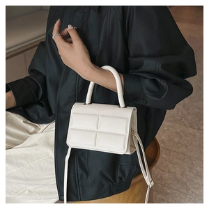 Detail of white quilted texture and gold hardware on minimalist crossbody handbag