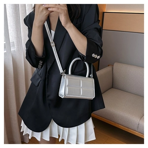 Silver metallic rectangular handbag worn over shoulder by model in black blazer
