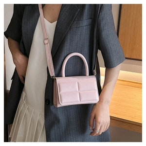 Detail of pink crossbody bag with square quilted texture and top handle on model