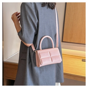 Detail of pink quilted crossbody bag with top handle worn over a grey blazer jacket