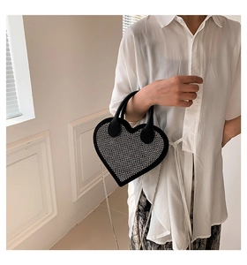 Detail of a heart-shaped black handbag featuring dense rhinestone embellishments and a metal chain