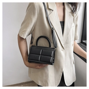 Chic black quilted crossbody bag with top handle worn on beige linen blazer jacket