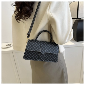 Detail van zwarte tas met geometrisch patroon, witte stiksels en een handvat boven