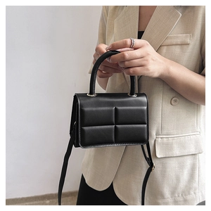 Detail of a black quilted leather square handbag with fixed handle and slim strap