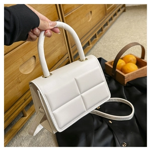 Detail view of the white quilted crossbody bag with golden hardware and hand strap