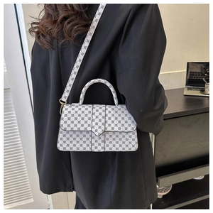 Witte crossbodytas met geometrisch patroon en goudkleurige details over een zwarte blazer
