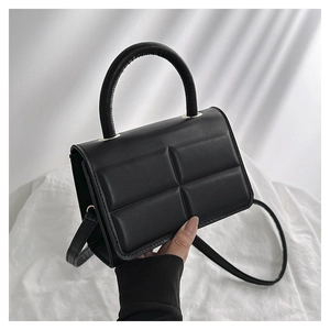 Detail of black quilted square handbag with cylindrical top handle and fine strap