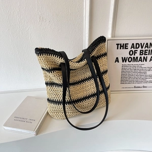 Woven straw tote bag with black stripes and leather straps in a minimalist lifestyle setting