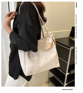 Detail of cream tote bag featuring houndstooth texture, woven handles, and decorative scarf