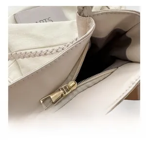 Detailed close-up of smooth gold metal zipper and crocodile embossed texture on a cream tote