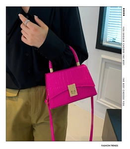 Detail of rose red faux leather crossbody bag featuring crocodile texture and golden clasp