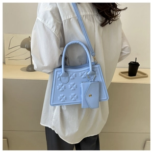 Detail van een lichtblauwe trapeze handtas met klaver reliëf en een kleine extra tas
