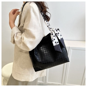 Detail of black tote bag featuring houndstooth texture and floral silk scarf on handle