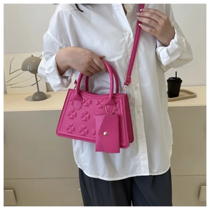Detail van rozerode crossbodytas met klaverreliëf en bijpassende kleine kaarthouder