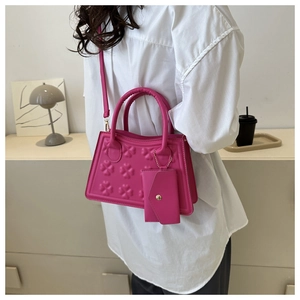 Detail van magenta handtas met klaverreliëf en afneembare kleine driehoekige tas