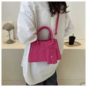 Detail van roze trapeze handtas met klaverbladreliëf en bijpassende mini tas hanger van leer