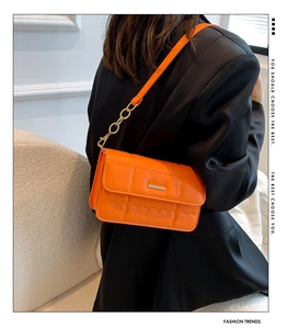 Detail van oranje gewatteerde crossbodytas met gouden hardware gedragen door model