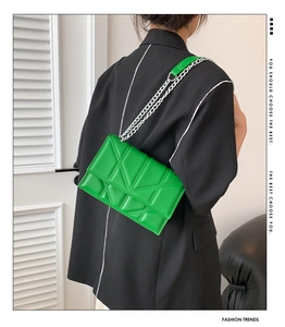 Detailed view of a bright green quilted crossbody bag with a silver chain strap on a model
