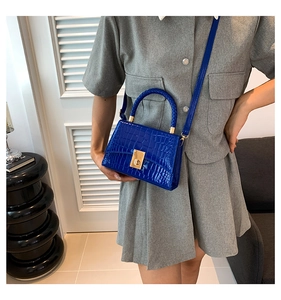 Detail of bright blue croc-effect leather handbag with gold clasp and woven handle