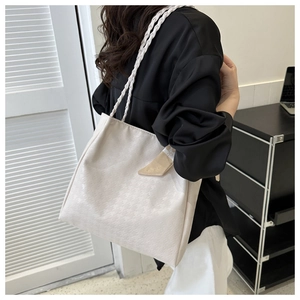 Detail of off-white tote bag with houndstooth pattern and braided rope strap worn by model