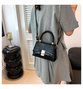 Model wearing black faux crocodile skin bag with golden twist lock and shoulder strap