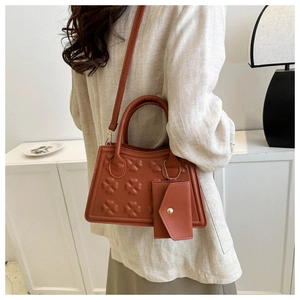 Detail van de karamel trapeze tas met klaver reliëf en een klein muntzakje aan de ketting