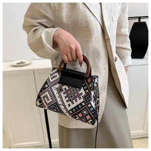 Close-up of geometric woven handbag featuring wooden handles and leather flap detail