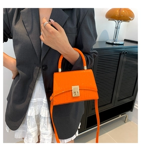 Detail of orange crocodile pattern crossbody bag with metallic lock shown on model