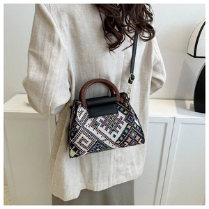 Detailed side view of a geometric woven handbag with wooden handles and a black leather flap