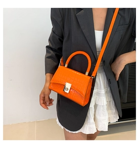 Model showing orange crocodile pattern crossbody bag with braided handle and metal twist lock