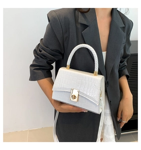 Close-up of a white croc-embossed handbag with gold twist lock and woven handle worn by model