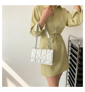 Side view of a white quilted geometric chain shoulder bag worn by a model in a minimalist setting