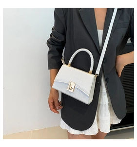 Close-up of white croc-effect leather handbag with gold twist lock and woven handle