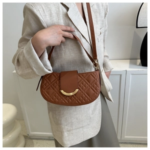 Detail van bruine gewatteerde zadeltas met gouden gesp op een beige blazer