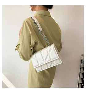 Detail of white quilted crossbody bag with silver chain strap shown on model's shoulder
