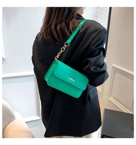 Detail van groene gewatteerde crossbodytas met gouden ketting over een zwarte blazer