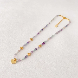 Collier de perles colorées avec pendentif cœur doré sur fond de pierre blanche