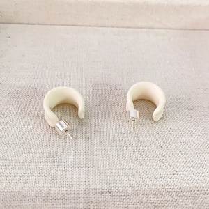 Minimalist C-shaped ivory enamel hoop earrings with silver pins on textured background