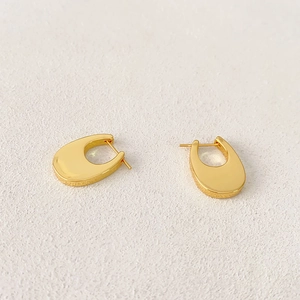 Polished U-shaped gold plated earrings set on a minimalist stone texture background