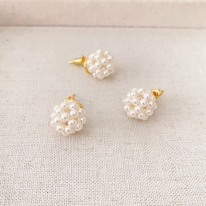Handcrafted pearl ball stud earrings with gold needles on white textured background