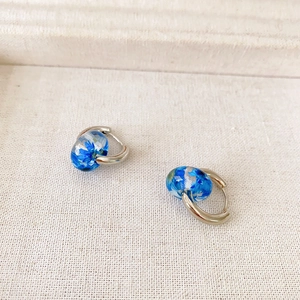 Close-up of hoop earrings with clear blue pendants containing dried floral elements