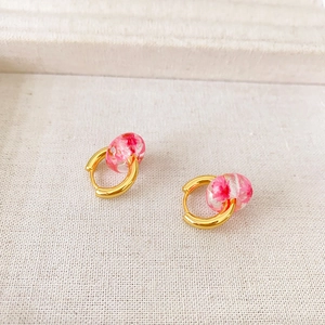Detailed macro of gold earrings with pink dried flowers in clear resin spheres