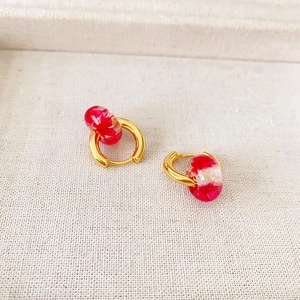 Detail of handmade gold earrings featuring red dried flowers inside transparent resin hoops