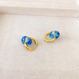 Detail of gold earrings with blue dried flower resin charms on white textured fabric