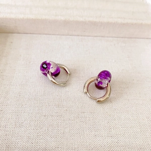 Silver hoop earrings with purple resin cylinders containing dried flowers on fabric