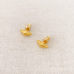 Close-up of golden croissant shaped earrings on textured beige linen background