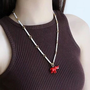 Detail of red elephant pendant necklace on a model wearing brown knitwear