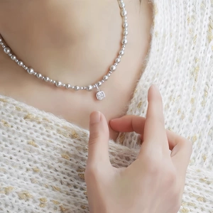 Elegant beaded necklace with square pavé pendant worn by model on white knit sweater