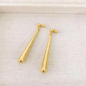 Macro shot of minimalist gold teardrop earrings on soft textured fabric background