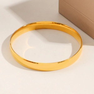Minimalist 8mm wide polished gold stainless steel bangle bracelet on beige surface